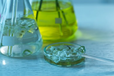 Photo of Making luxury perfume. Essential oils in glassware and flowers on white wooden table, closeup