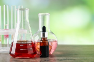 Photo of Making luxury perfume. Essential oils in glassware and flowers on wooden table against blurred background, closeup. Space for text