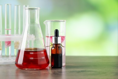 Photo of Making luxury perfume. Essential oils in glassware and flowers on wooden table against blurred background, closeup. Space for text