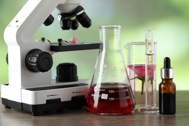 Photo of Making luxury perfume. Essential oils in glassware and flowers on wooden table against blurred background, closeup