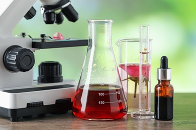 Photo of Making luxury perfume. Essential oils in glassware and flowers on wooden table against blurred background, closeup