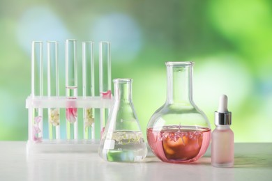 Photo of Making luxury perfume. Essential oils in glassware and flowers on white wooden table against blurred background