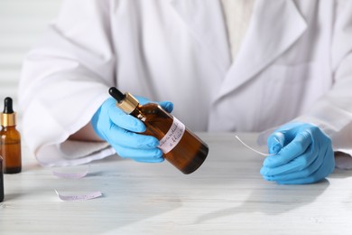 Photo of Professional perfumer developing luxury perfume at white wooden table in laboratory, closeup