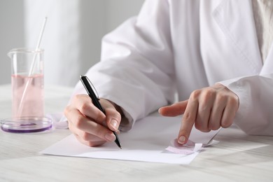 Photo of Professional perfumer developing luxury perfume at white wooden table in laboratory, closeup