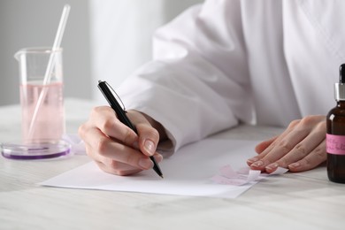 Photo of Professional perfumer developing luxury perfume at white wooden table in laboratory, closeup
