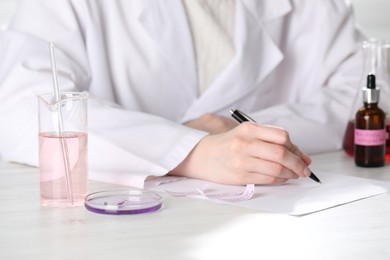 Photo of Professional perfumer developing luxury perfume at white wooden table in laboratory, closeup
