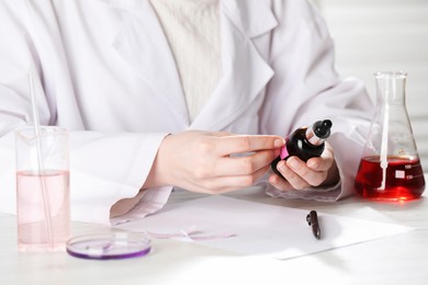 Photo of Professional perfumer developing luxury perfume at white wooden table in laboratory, closeup