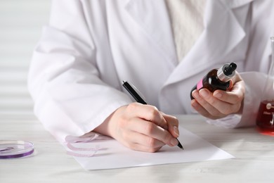 Photo of Professional perfumer developing luxury perfume at white wooden table in laboratory, closeup
