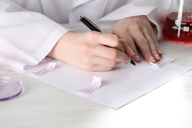 Photo of Professional perfumer developing luxury perfume at white wooden table in laboratory, closeup