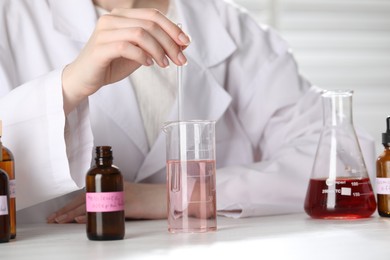 Photo of Professional perfumer developing luxury perfume at white wooden table in laboratory, closeup
