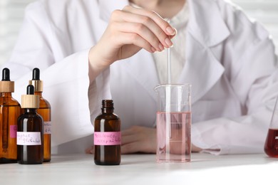 Photo of Professional perfumer developing luxury perfume at white wooden table in laboratory, closeup