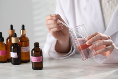 Photo of Professional perfumer developing luxury perfume at white wooden table in laboratory, closeup