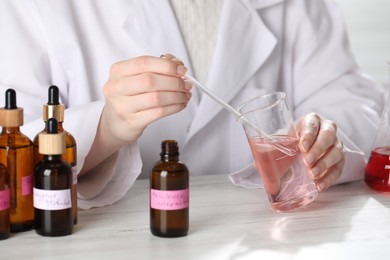 Photo of Professional perfumer developing luxury perfume at white wooden table in laboratory, closeup