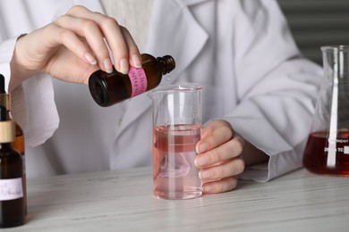 Photo of Professional perfumer developing luxury perfume at white wooden table in laboratory, closeup