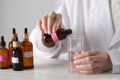 Photo of Professional perfumer developing luxury perfume at white wooden table in laboratory, closeup