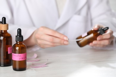 Photo of Professional perfumer developing luxury perfume at white wooden table in laboratory, closeup