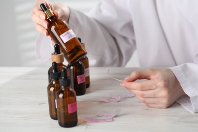 Photo of Professional perfumer developing luxury perfume at white wooden table in laboratory, closeup