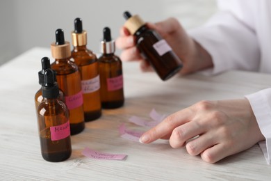 Photo of Professional perfumer developing luxury perfume at white wooden table in laboratory, closeup