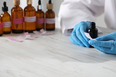 Photo of Professional perfumer developing luxury perfume at white wooden table in laboratory, closeup