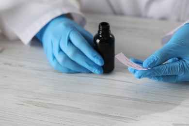 Photo of Professional perfumer developing luxury perfume at white wooden table in laboratory, closeup
