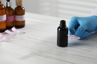 Photo of Professional perfumer developing luxury perfume at white wooden table in laboratory, closeup