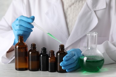 Photo of Professional perfumer developing luxury perfume at white wooden table in laboratory, closeup