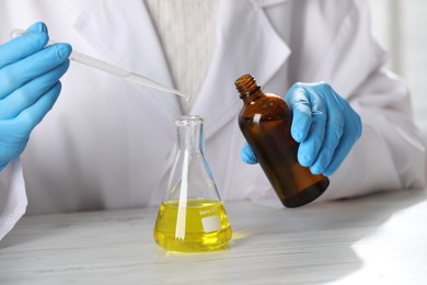 Photo of Professional perfumer developing luxury perfume at white wooden table in laboratory, closeup