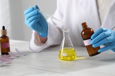 Photo of Professional perfumer developing luxury perfume at white wooden table in laboratory, closeup