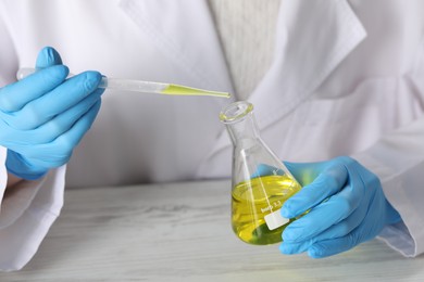 Photo of Professional perfumer developing luxury perfume at white wooden table in laboratory, closeup