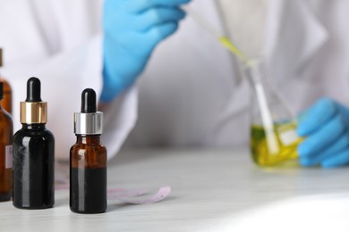 Photo of Professional perfumer developing luxury perfume at white wooden table in laboratory, closeup