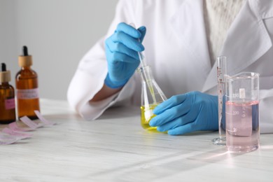 Photo of Professional perfumer developing luxury perfume at white wooden table in laboratory, closeup