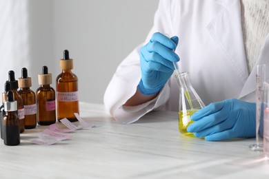 Photo of Professional perfumer developing luxury perfume at white wooden table in laboratory, closeup
