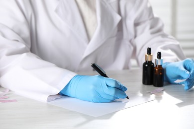 Photo of Professional perfumer developing luxury perfume at white wooden table in laboratory, closeup
