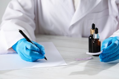 Photo of Professional perfumer developing luxury perfume at white wooden table in laboratory, closeup