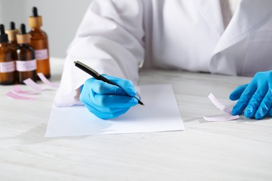 Photo of Professional perfumer developing luxury perfume at white wooden table in laboratory, closeup