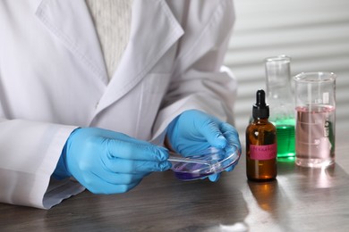 Photo of Professional perfumer developing luxury perfume at wooden table in laboratory, closeup