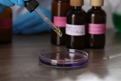 Photo of Professional perfumer developing luxury perfume at wooden table in laboratory, closeup