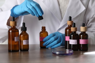 Photo of Professional perfumer developing luxury perfume at wooden table in laboratory, closeup