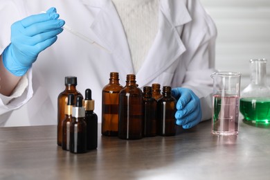 Photo of Professional perfumer developing luxury perfume at wooden table in laboratory, closeup