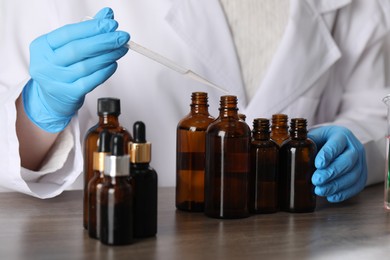 Photo of Professional perfumer developing luxury perfume at wooden table in laboratory, closeup