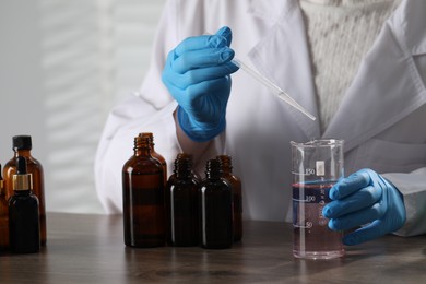 Photo of Professional perfumer developing luxury perfume at wooden table in laboratory, closeup