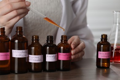 Photo of Professional perfumer developing luxury perfume at wooden table in laboratory, closeup