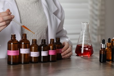 Photo of Professional perfumer developing luxury perfume at wooden table in laboratory, closeup
