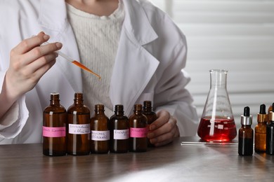 Photo of Professional perfumer developing luxury perfume at wooden table in laboratory, closeup