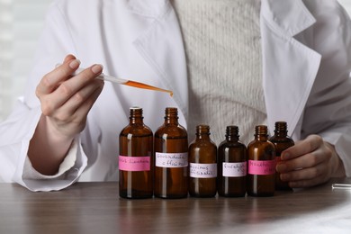 Photo of Professional perfumer developing luxury perfume at wooden table in laboratory, closeup