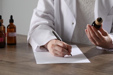 Photo of Professional perfumer developing luxury perfume at wooden table in laboratory, closeup