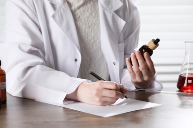 Photo of Professional perfumer developing luxury perfume at wooden table in laboratory, closeup