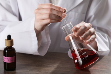 Photo of Professional perfumer developing luxury perfume at wooden table in laboratory, closeup