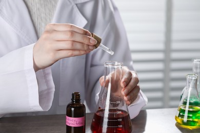 Photo of Professional perfumer developing luxury perfume at wooden table in laboratory, closeup