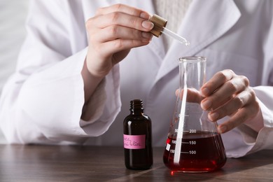 Photo of Professional perfumer developing luxury perfume at wooden table in laboratory, closeup